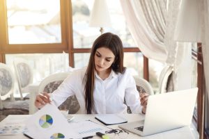 Young brunette business lady is analyzing diagrammes and working on the laptop