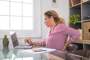 Close up rear view stressed young woman touching lower back feeling discomfort, suffering from sudden pain due to sedentary lifestyle or long computer overwork in incorrect posture at home office.