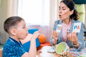 The attractive woman teacher teaches the preschool aged boy to read. The woman is holding the cards with the letters and the boy is trying to read them (The attractive woman teacher teaches the preschool aged boy to read. The woman is holding the card